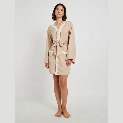 Woman wearing a beige robe with white lace trim on a plain background