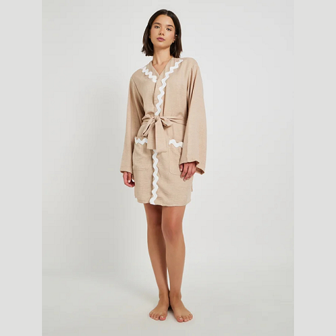 Woman wearing a beige robe with white lace trim on a plain background